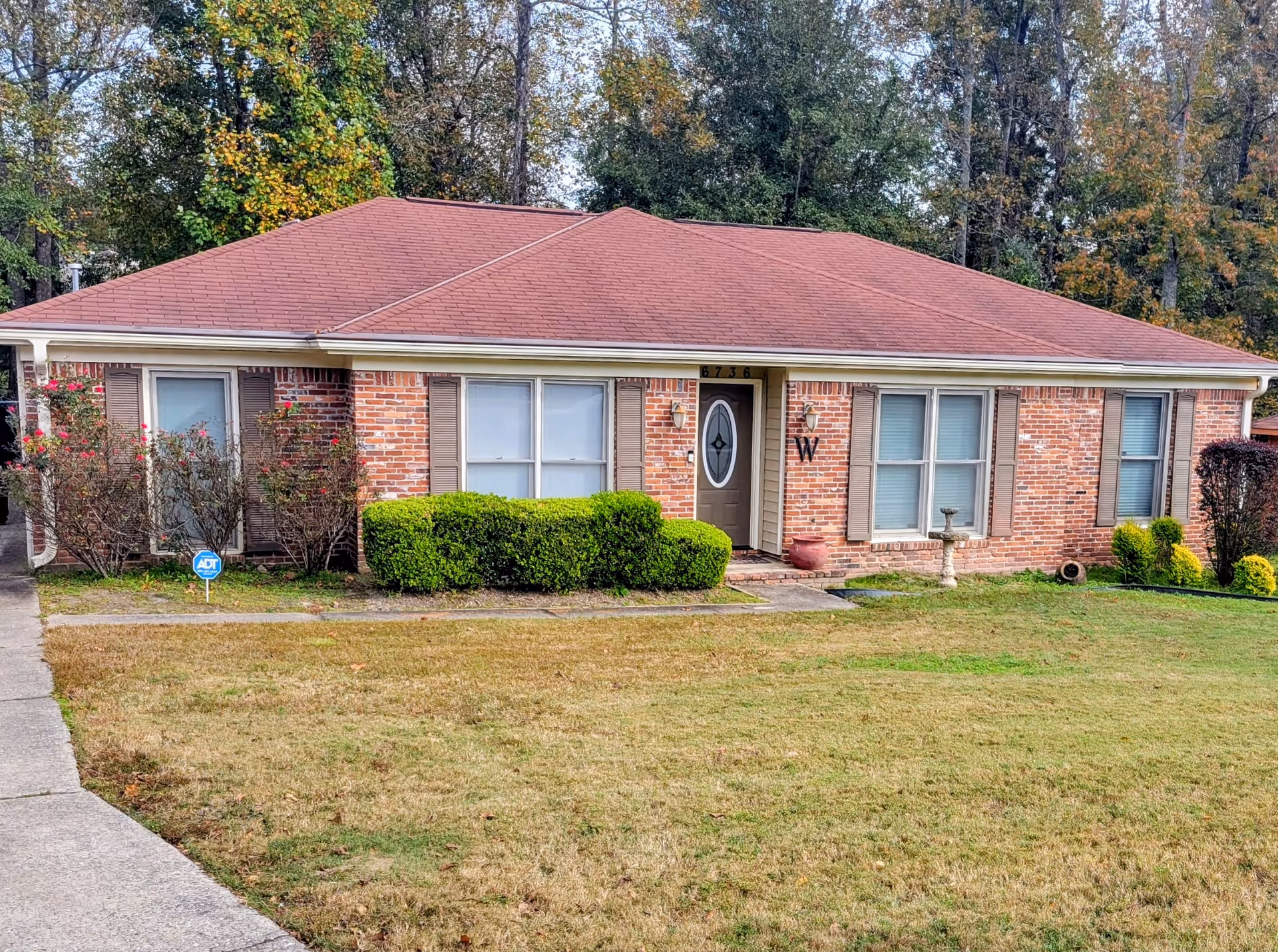 Single-story brick care home with a red roof, front yard, and trimmed shrubs.