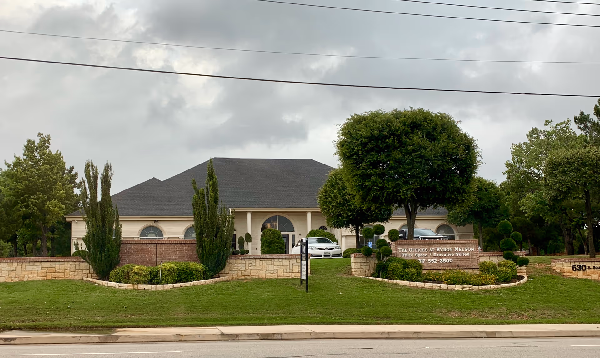 Single-story office-style building with arched windows, landscaping, and a front sign in a suburban lot.