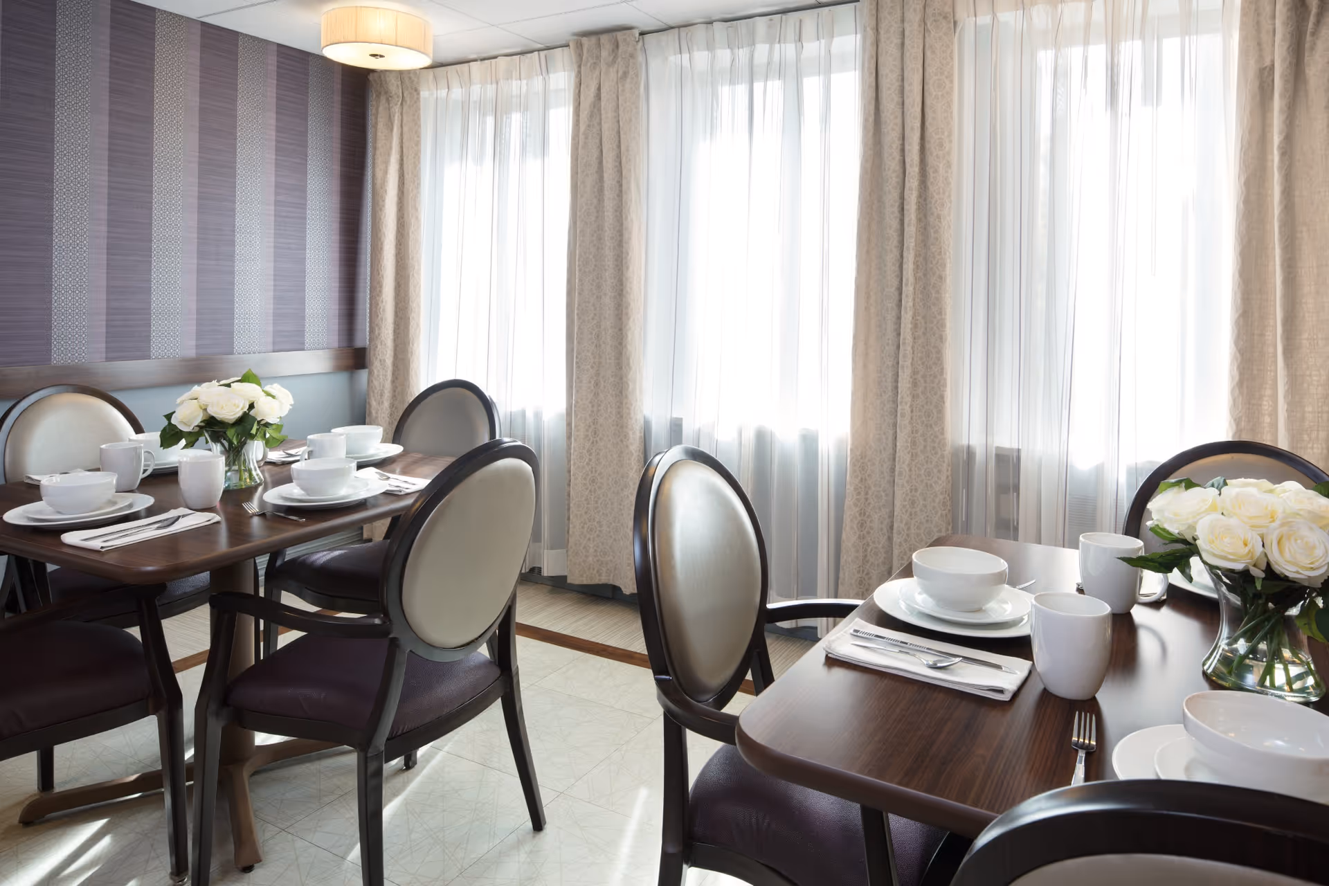 Dining room with wooden tables set with dishes, cups, and floral centerpieces.