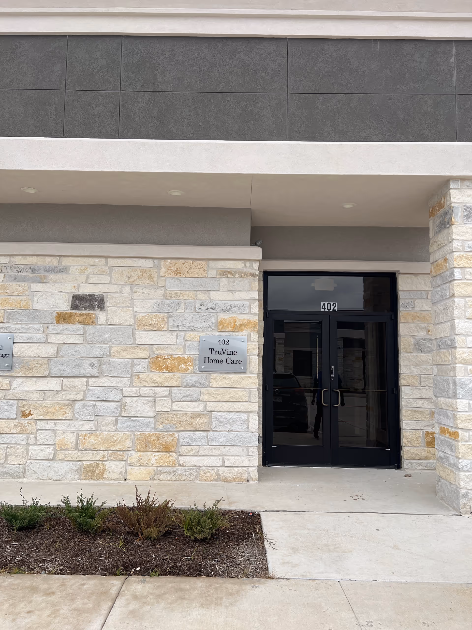 Exterior stone facade of TruVine Home Care with dark glass entry doors.