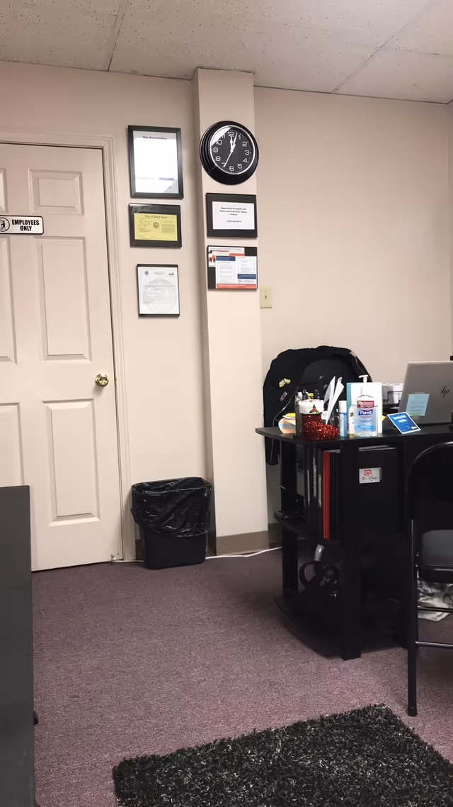Office desk area in a facility with clock, certificates, and a trash can.