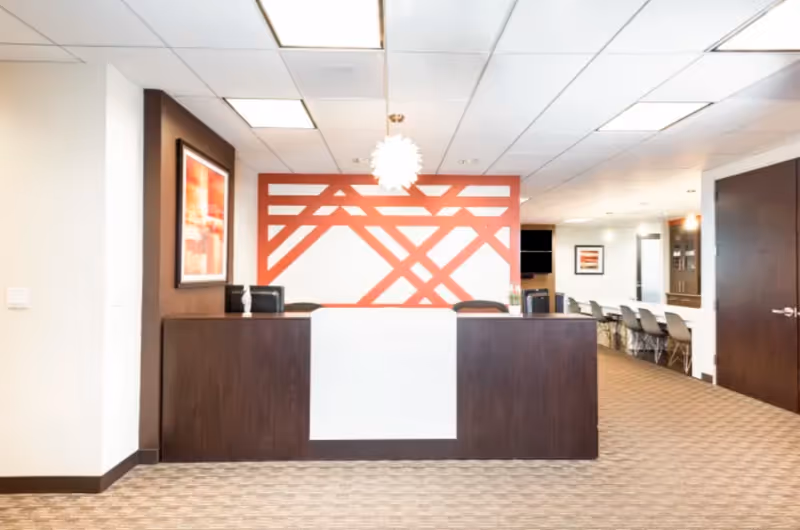 Lobby reception desk with red geometric wall art and seating beyond in a modern facility.