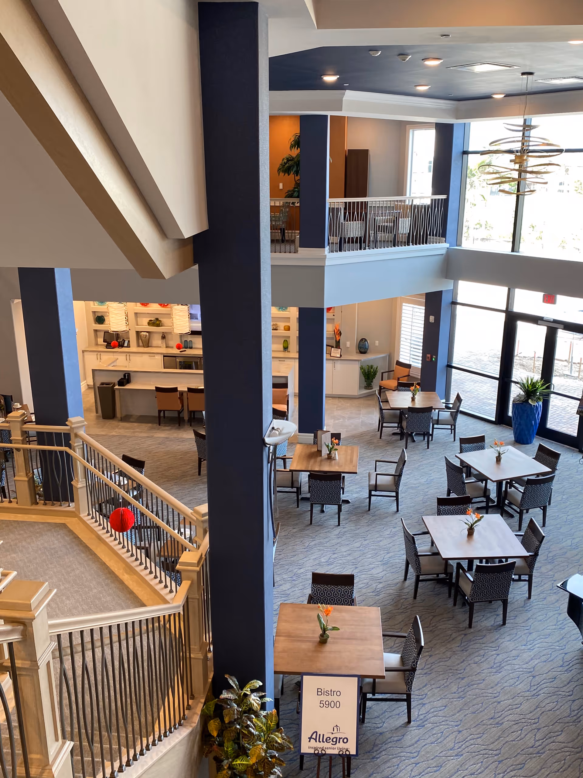 Open dining area in a senior living facility with blue pillars, tables, chairs, and a stairwell.