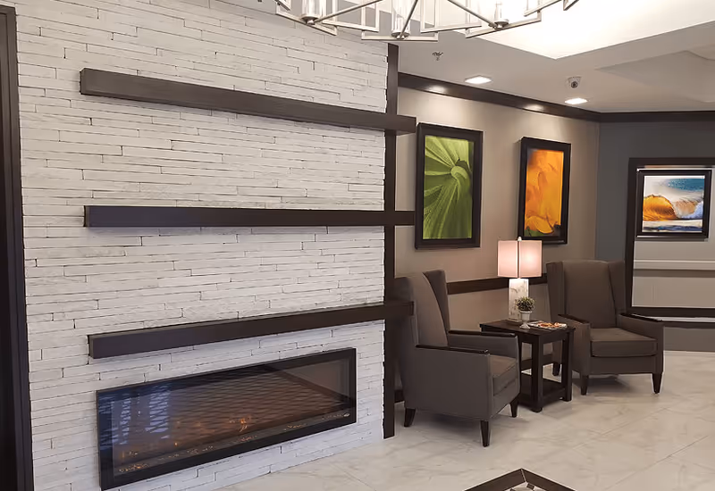 Modern seating area with a long linear fireplace set in a white stacked-stone wall, two upholstered armchairs and a side table beneath framed artwork.