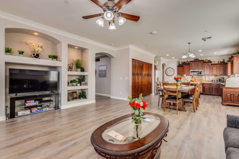 Open-concept living area with TV, built-in shelves, dining table, and large wooden kitchen cabinets.