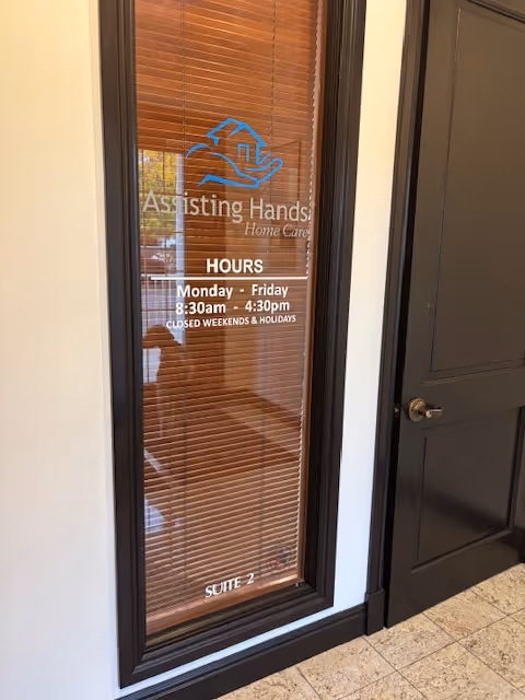Glass doorway with blinds and Assisting Hands Home Care branding in a hallway