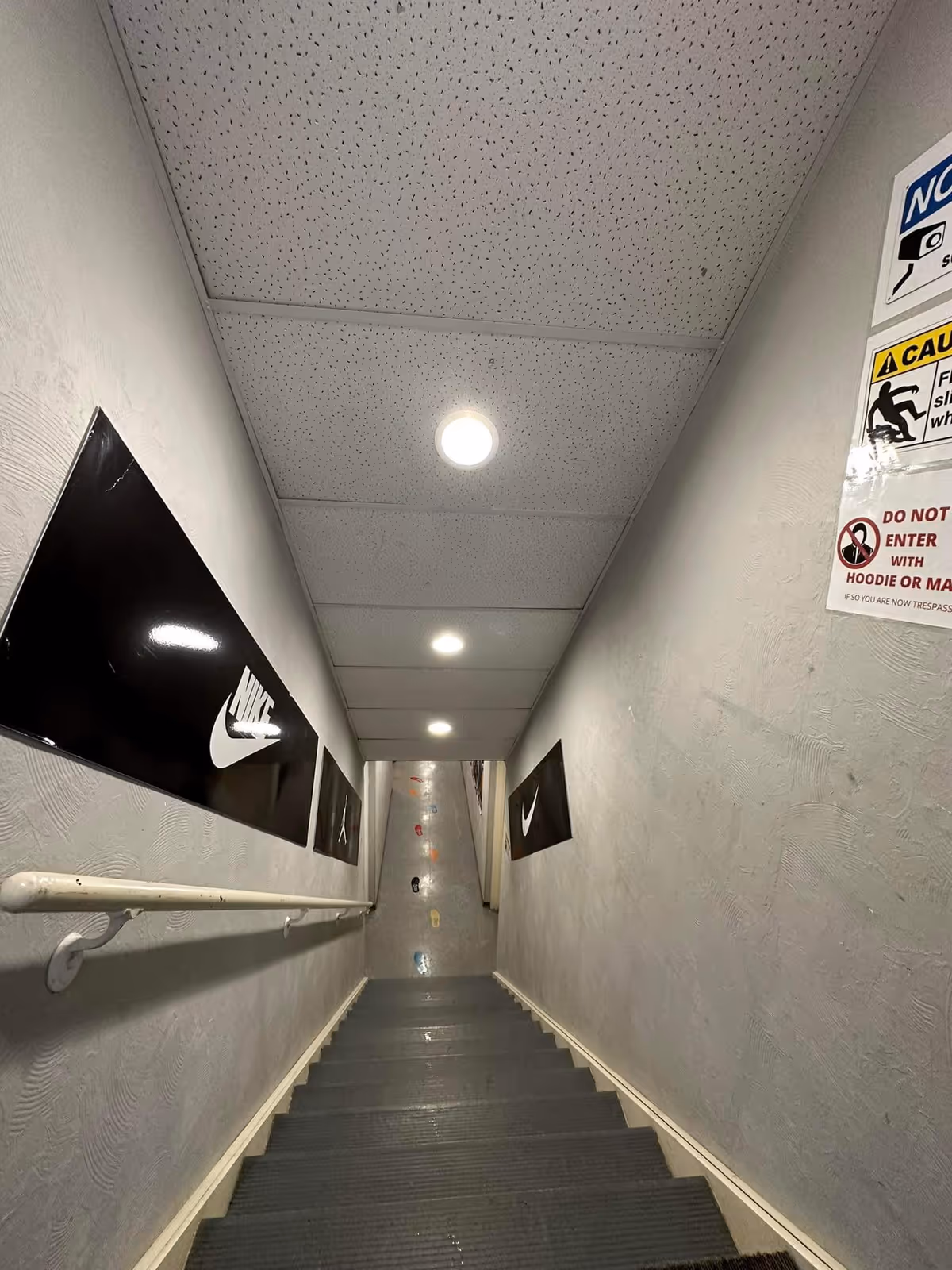 Narrow indoor stairwell with gray steps, white walls, and Nike wall panels.