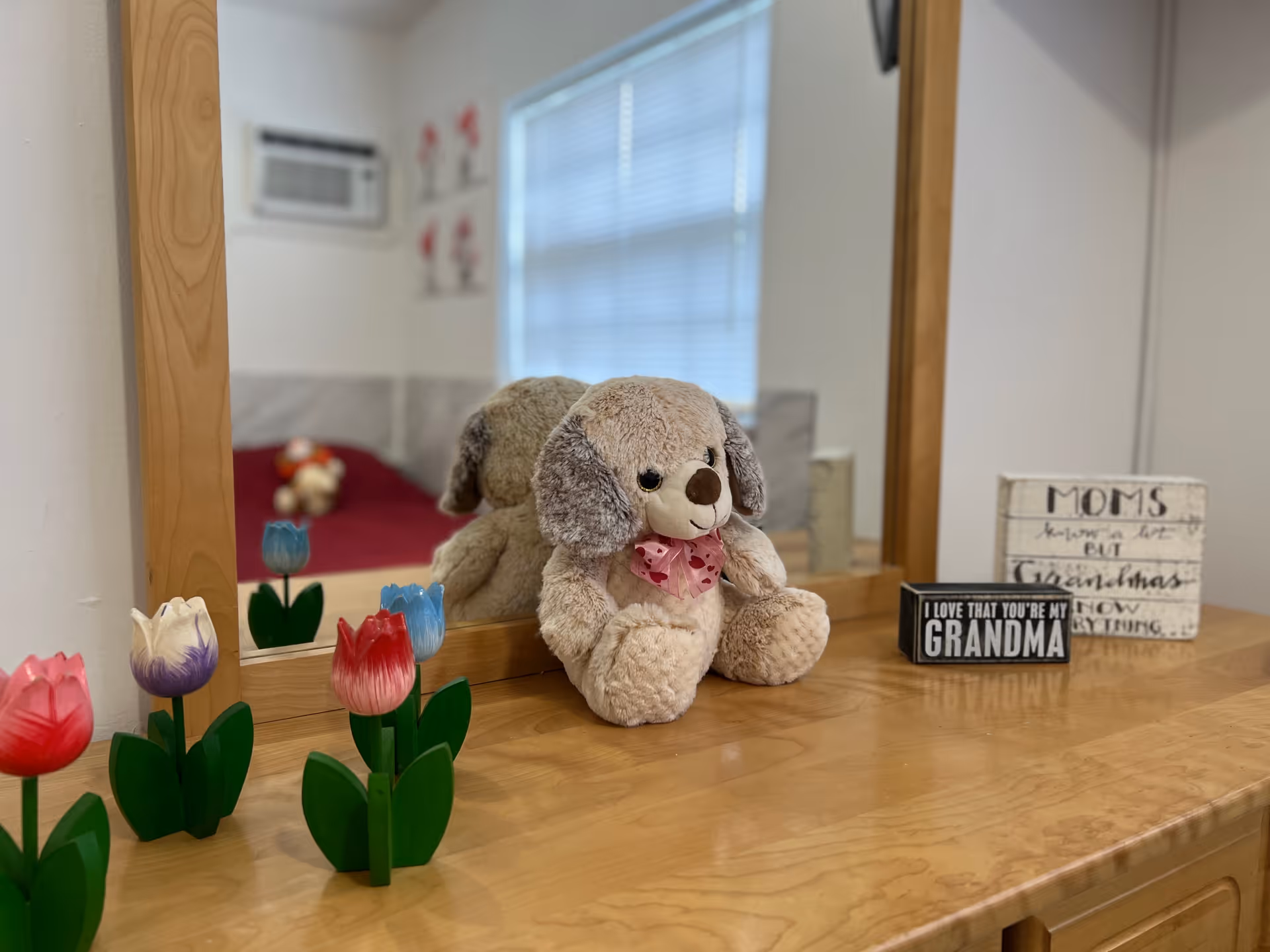 A stuffed dog sits on a dresser with tulips and a grandma sign.
