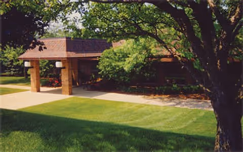 Exterior view of Farmington Hills Inn Assisted Living with a covered entrance, trees, and lawn.