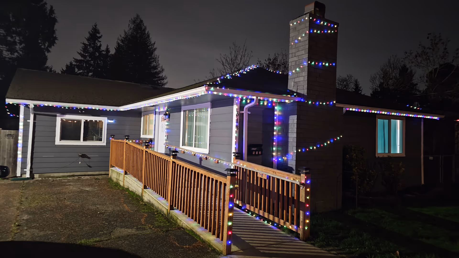 A single-story, house-style senior care facility at night with colorful string lights along the railing.