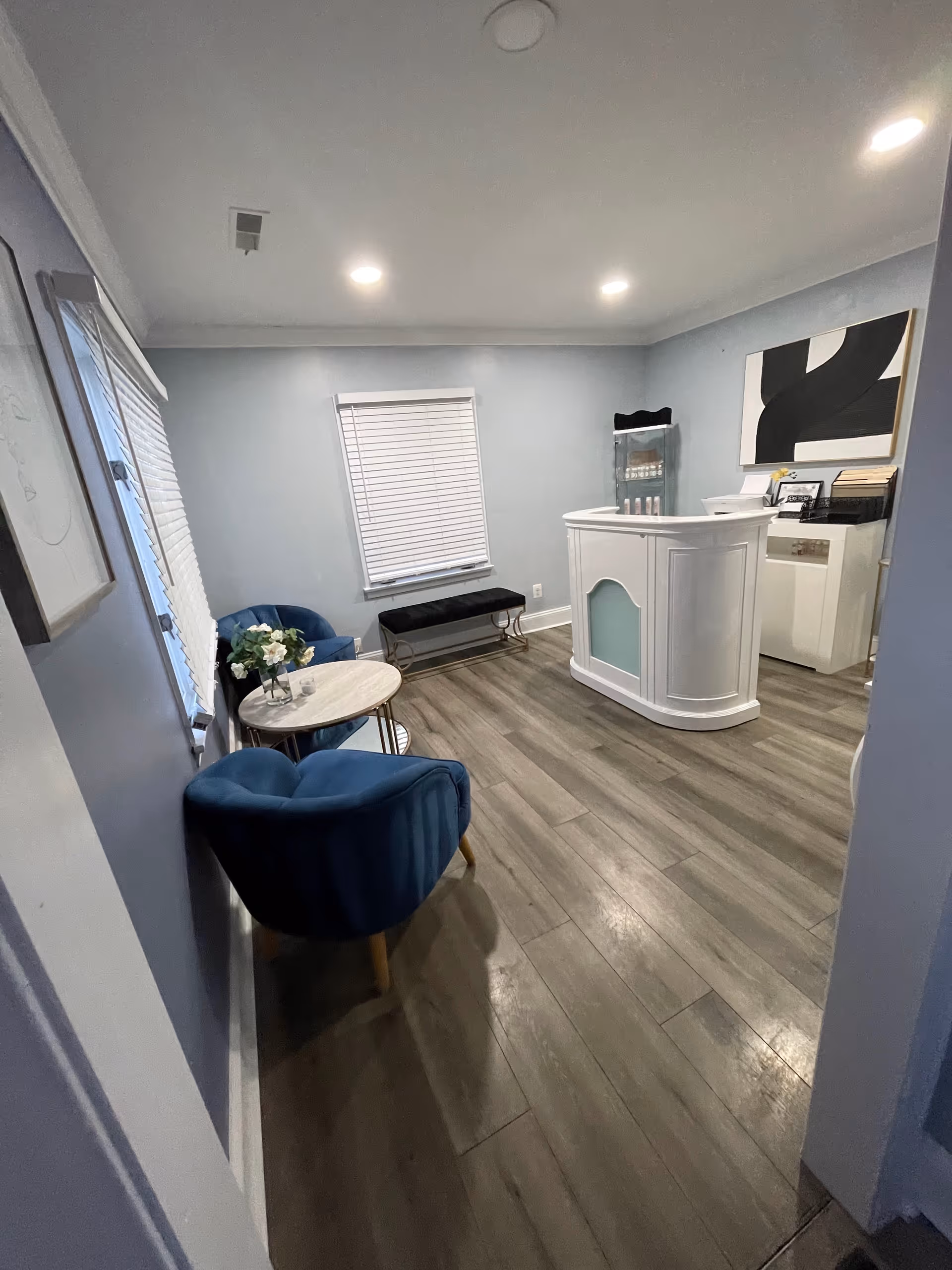 Reception lounge with blue chairs, a small table, and a white curved front desk.