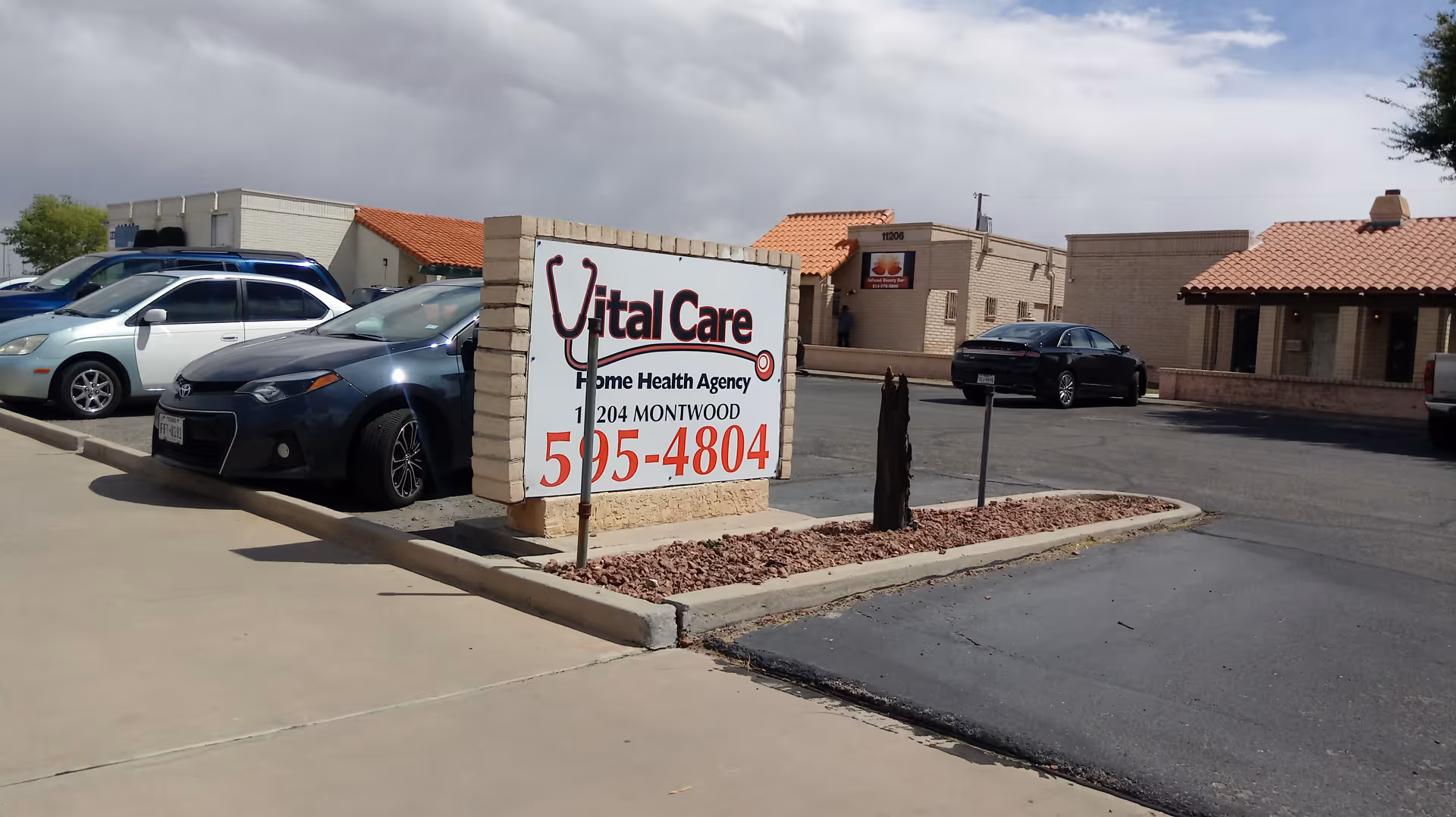 Exterior view of Vital Care facility with sign and parked cars.