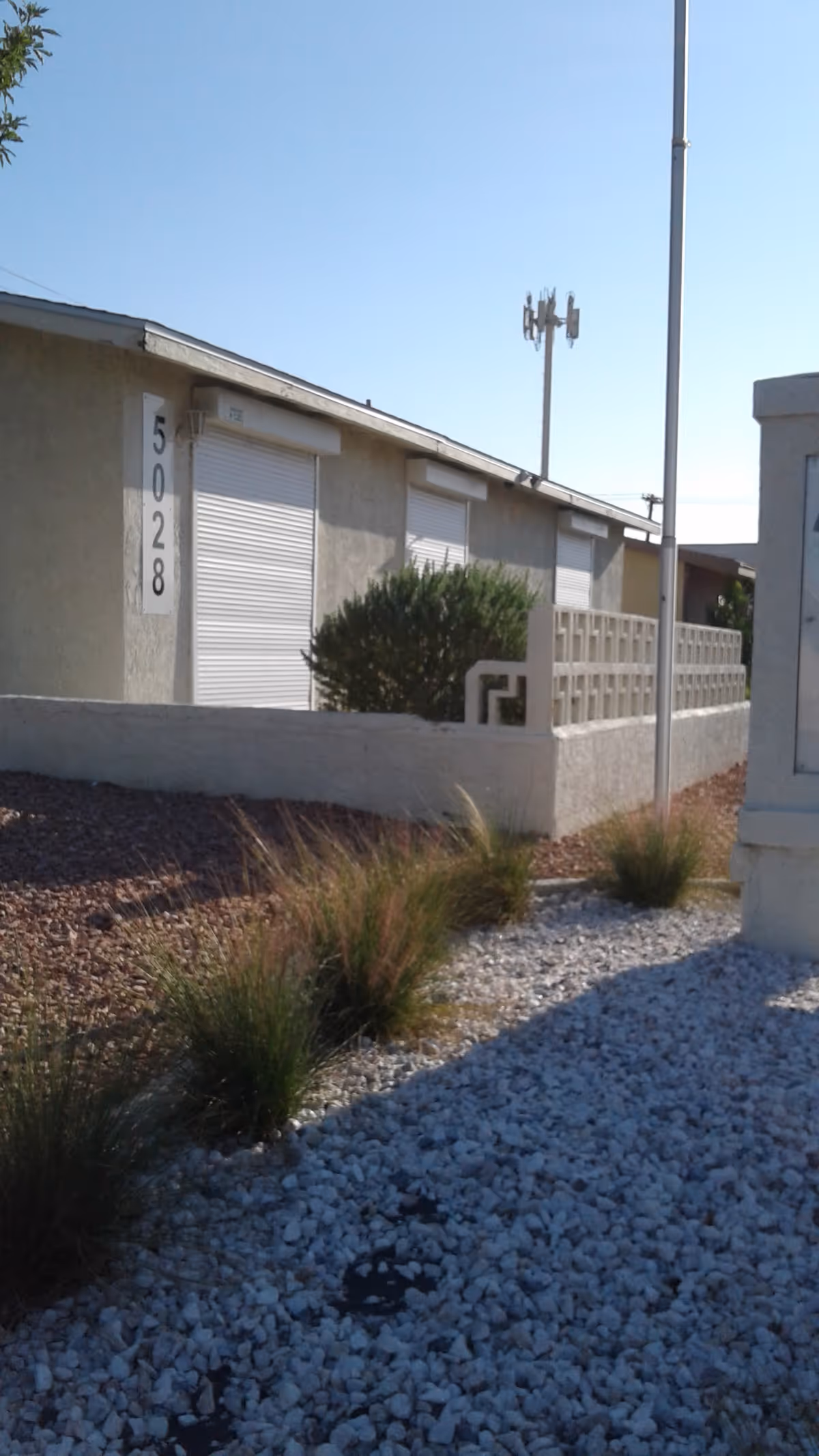 Exterior view of a beige senior living facility with gravel landscaping and low shrubs.