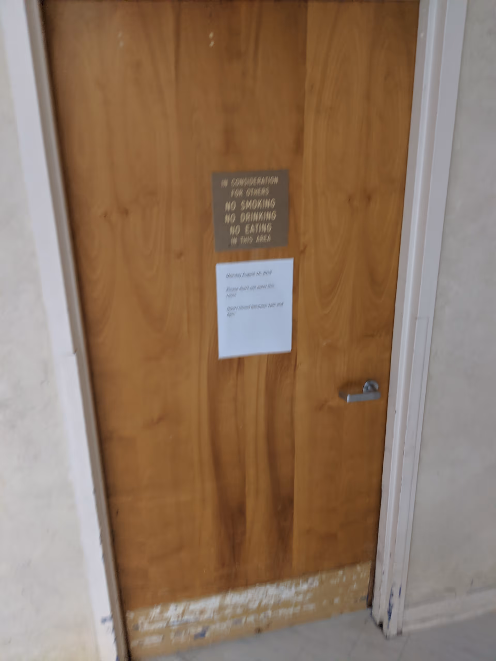 Wooden door with posted signs in a hallway of a senior facility.