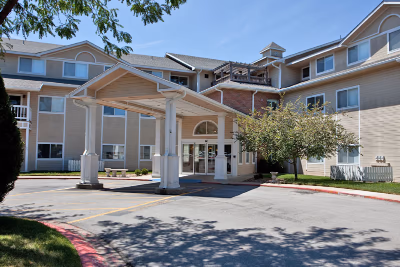 Covered entrance and porte-cochère of a beige multi-story senior living building with driveway and landscaping.