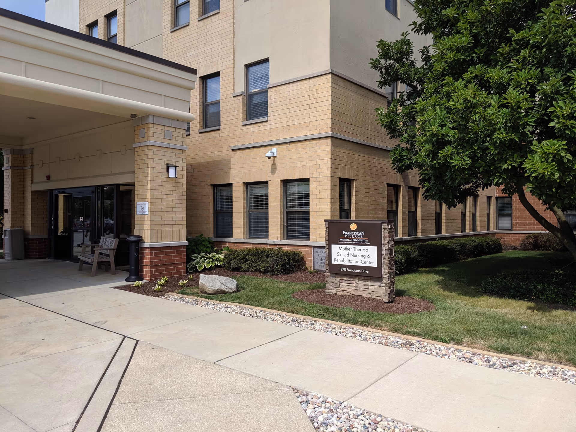 Exterior view of Mother Theresa Home senior living facility entrance with sign and landscaping