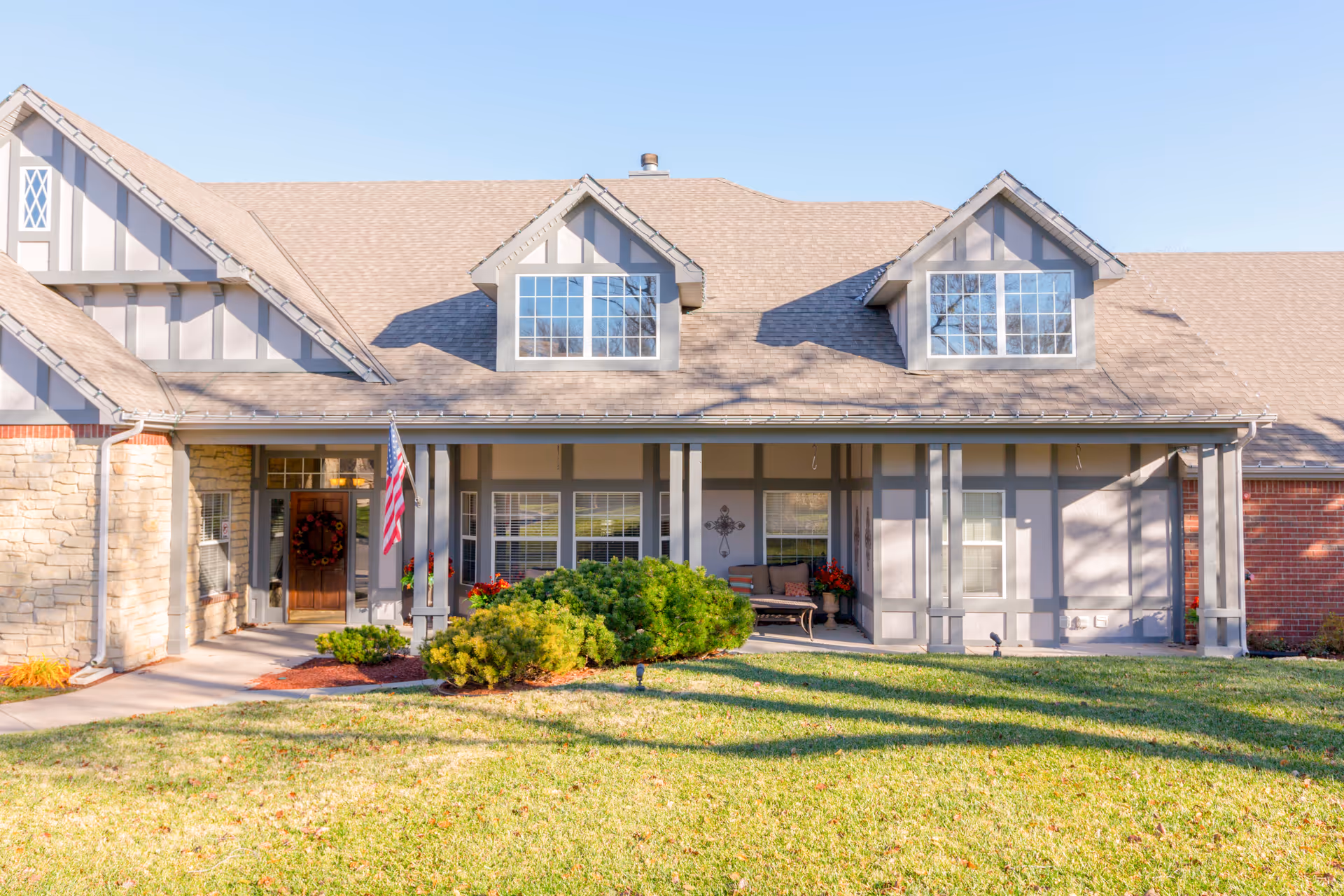 Front exterior of a Brookdale Tallgrass building with a porch, lawn, and flag.