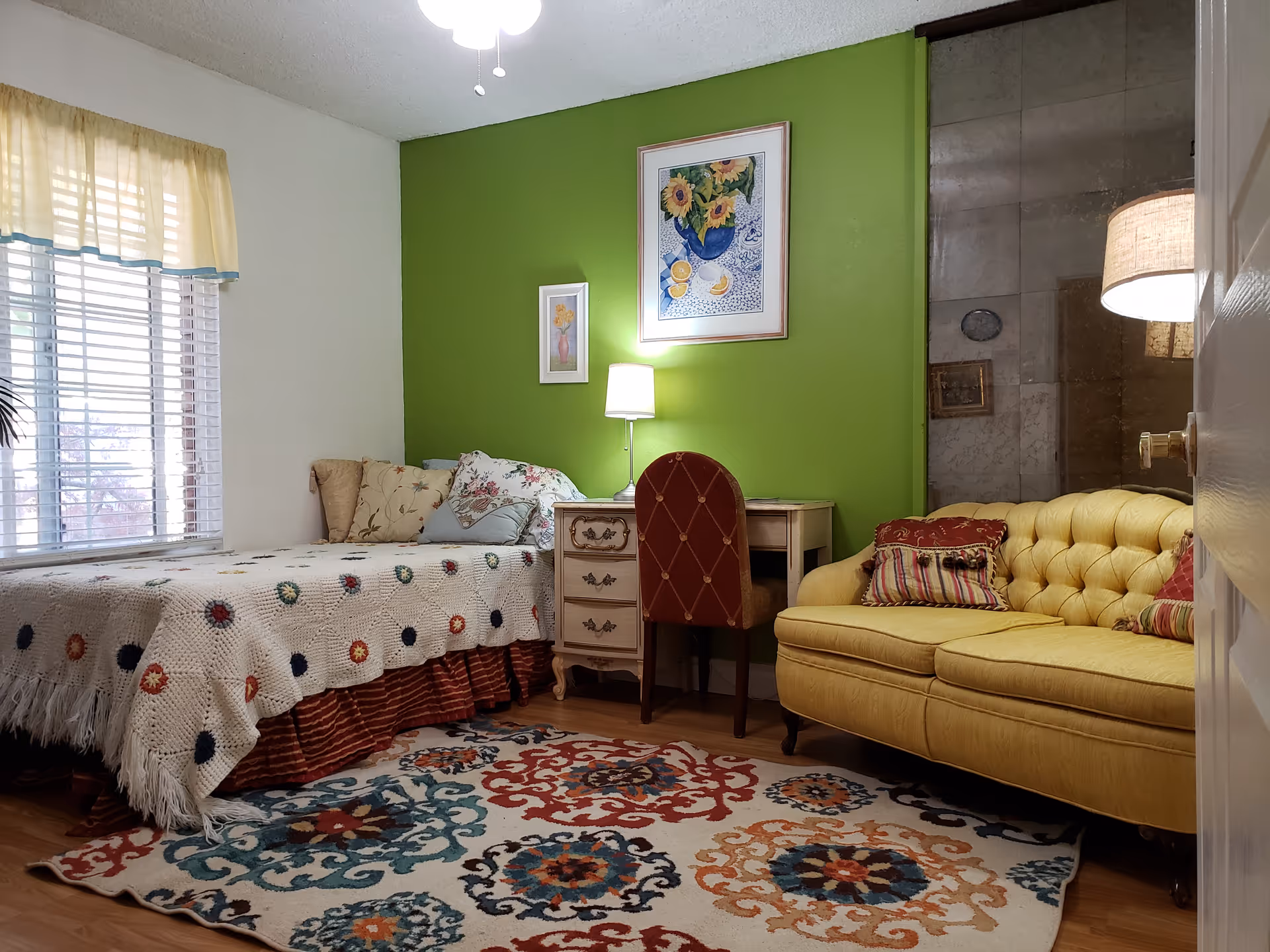 Cozy interior with a bed, desk, yellow sofa, vibrant rug, and green accent wall.
