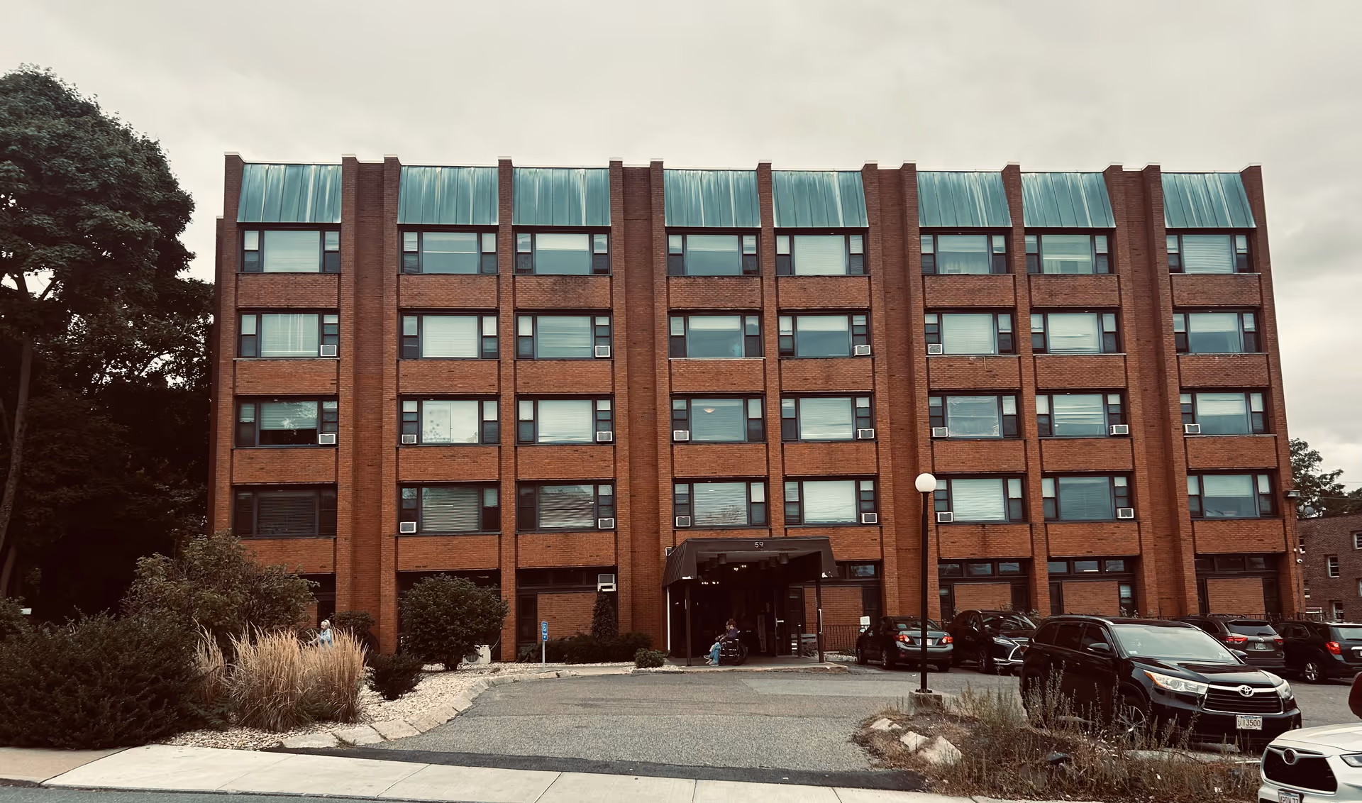 Watertown Health Center building, brick exterior with many windows and a dark entrance, parking in front.