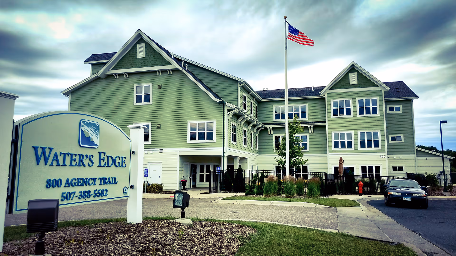 Exterior view of Water's Edge senior living building with sign and flag