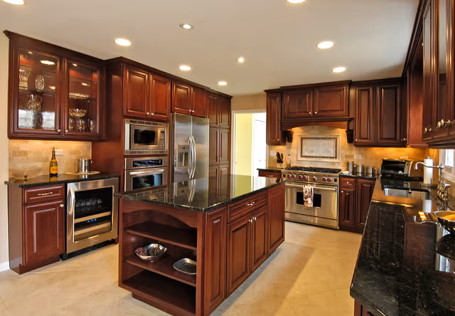 Spacious kitchen with dark wood cabinetry, a central island with a dark granite countertop, and stainless steel appliances.