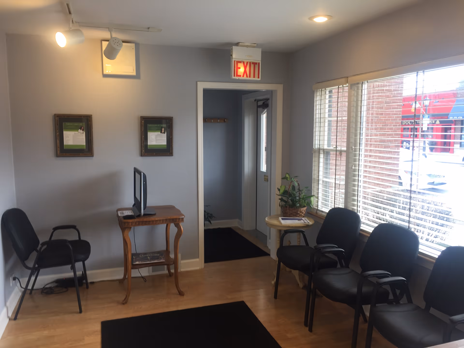 A small clinic waiting area with chairs, a window, and an exit sign.