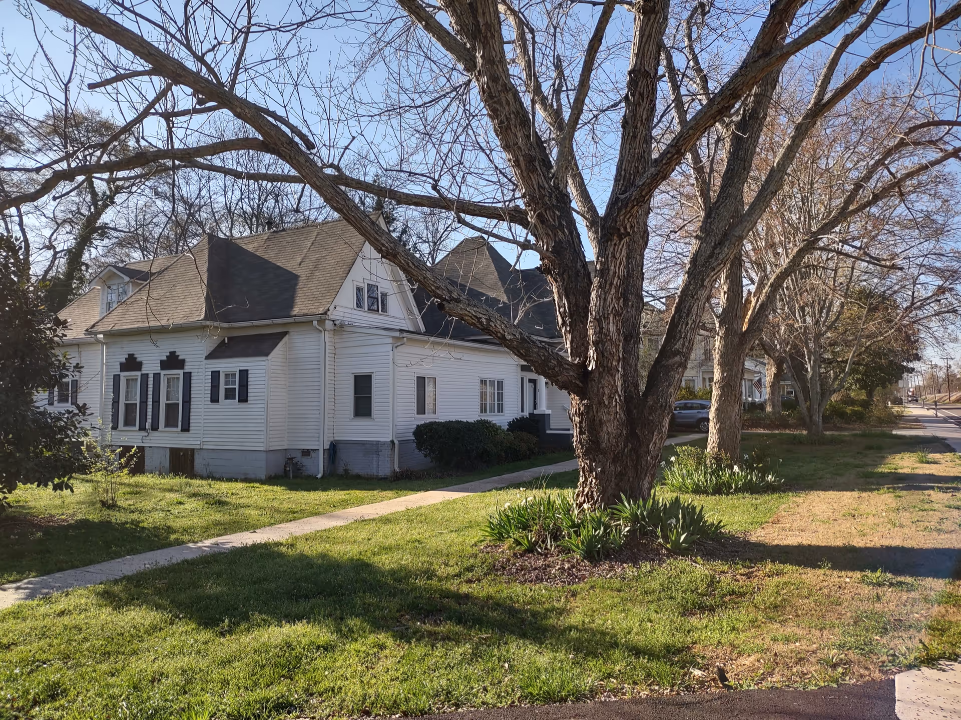 White wooden building exterior with trees lining a sidewalk and grassy lawn
