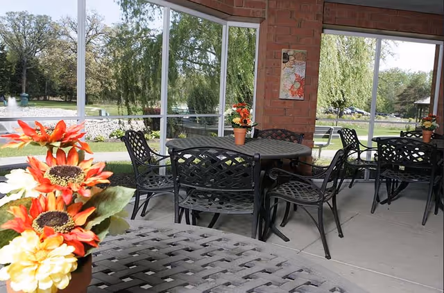 Screened outdoor patio with metal tables and chairs, potted flower arrangements, and a view of the lawn and trees.