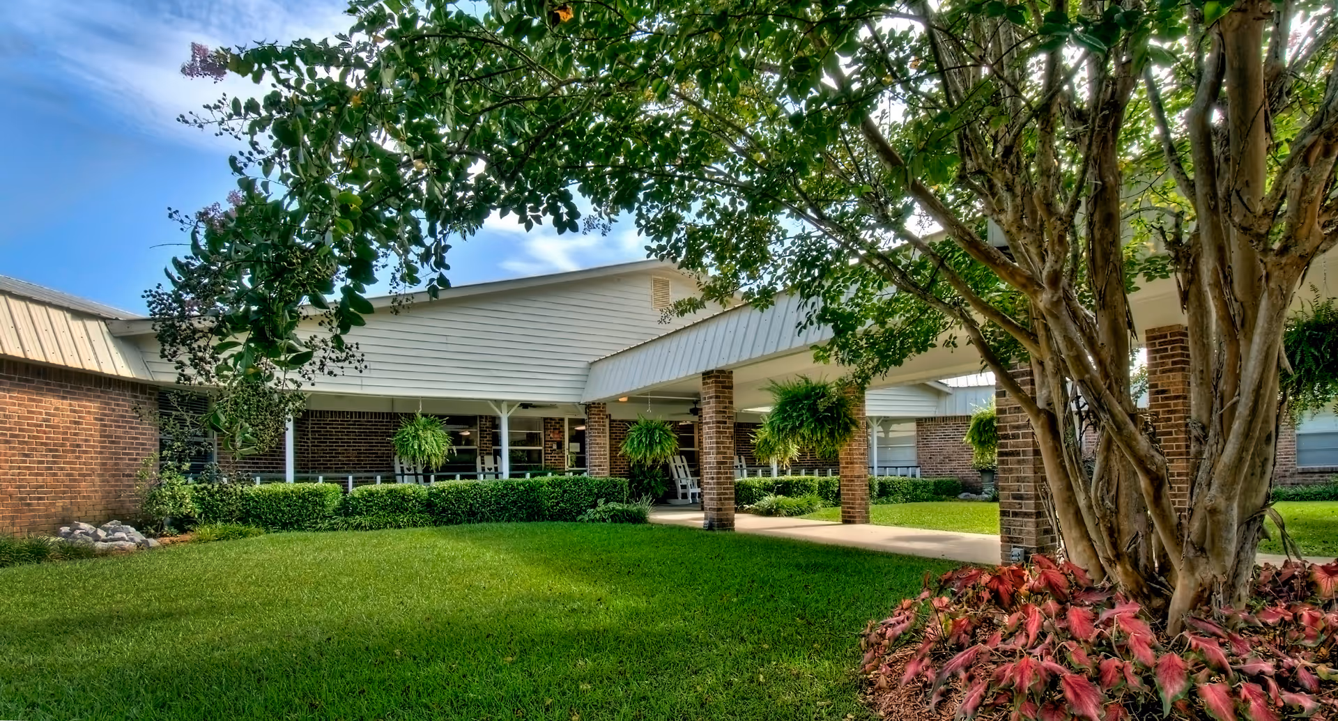 Brick senior living facility with covered entrance, columns, and lush landscaping.