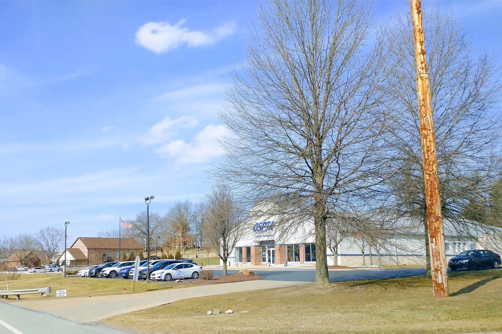 Exterior view of Ospta At Home facility with parking lot and trees.
