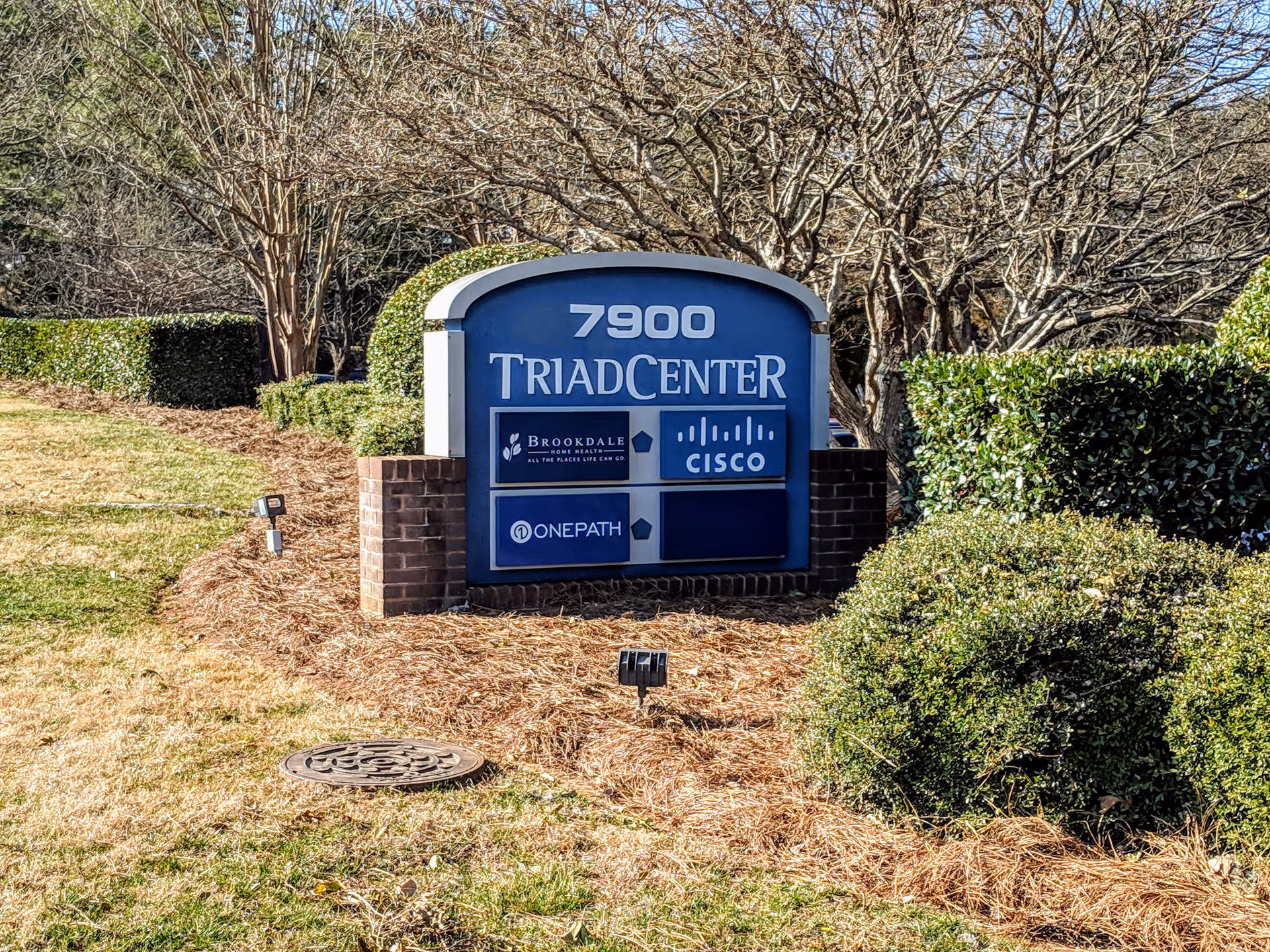 Exterior sign for 7900 TriadCenter with logos, surrounded by landscaping.