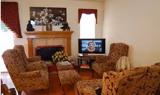 Cozy living room in a senior facility with patterned chairs, fireplace, and TV.