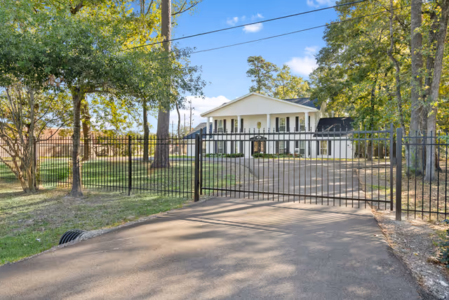 Gated driveway leads to a single-story senior living facility surrounded by trees.