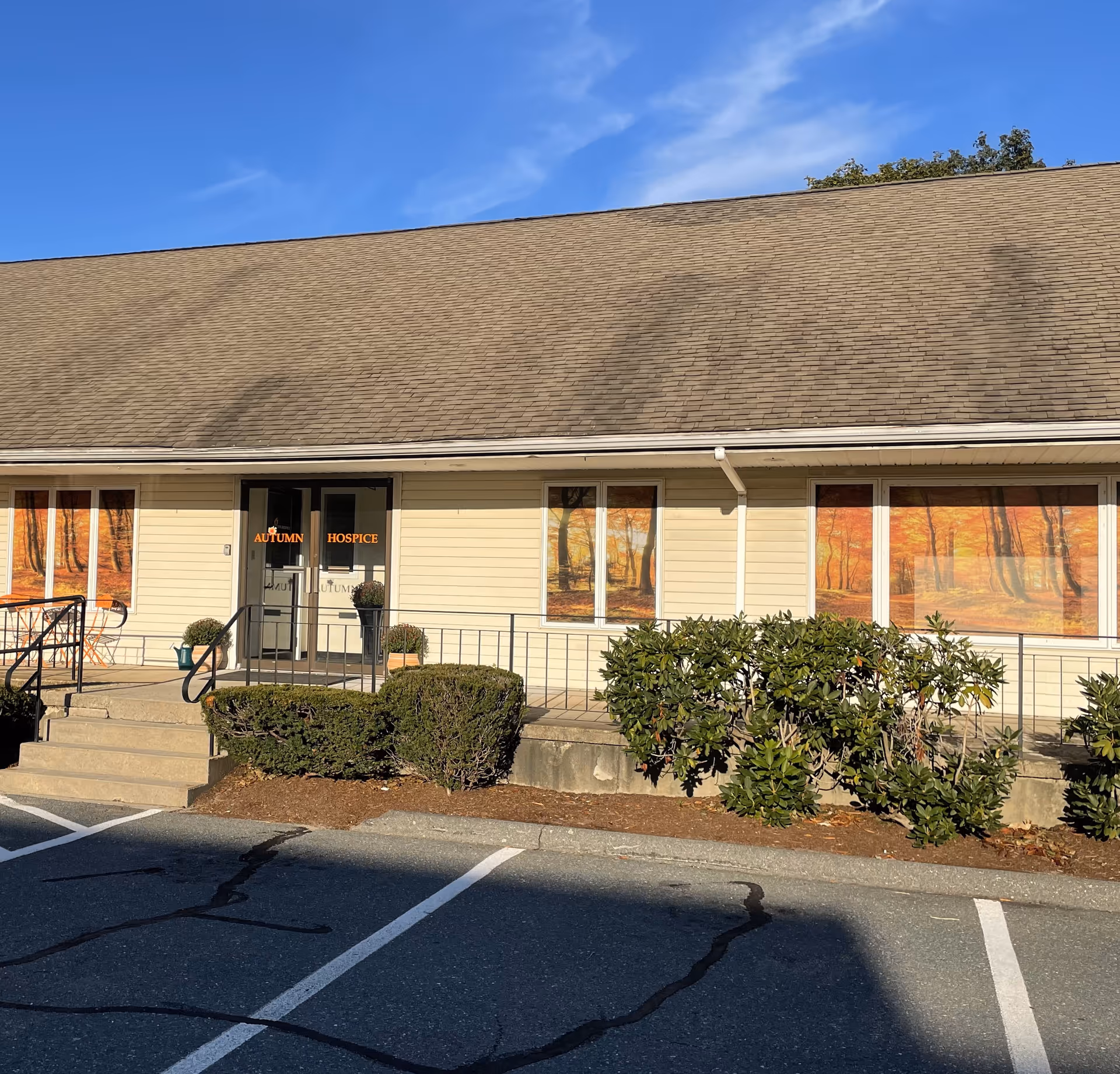 Exterior of Autumn Hospice building with entrance, windows, shrubs, and a parking lot.