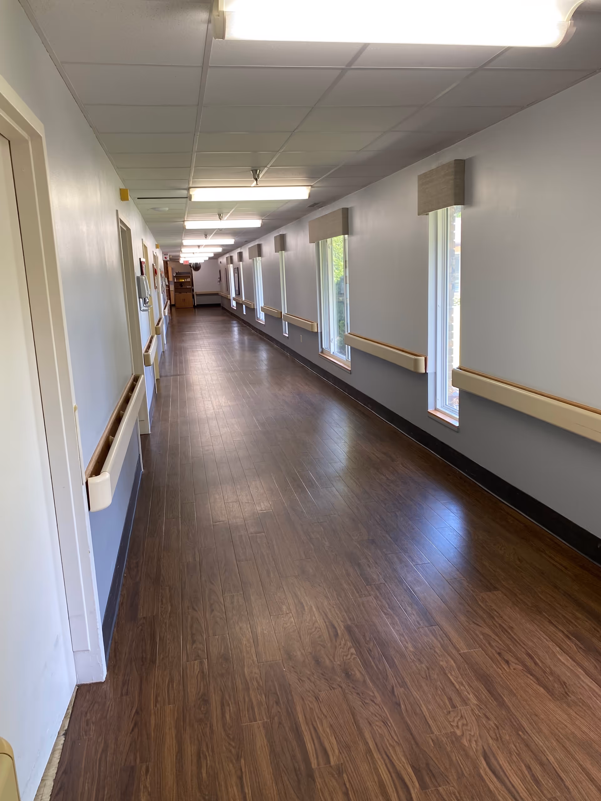 Interior corridor in a senior living facility with wood flooring and handrails.