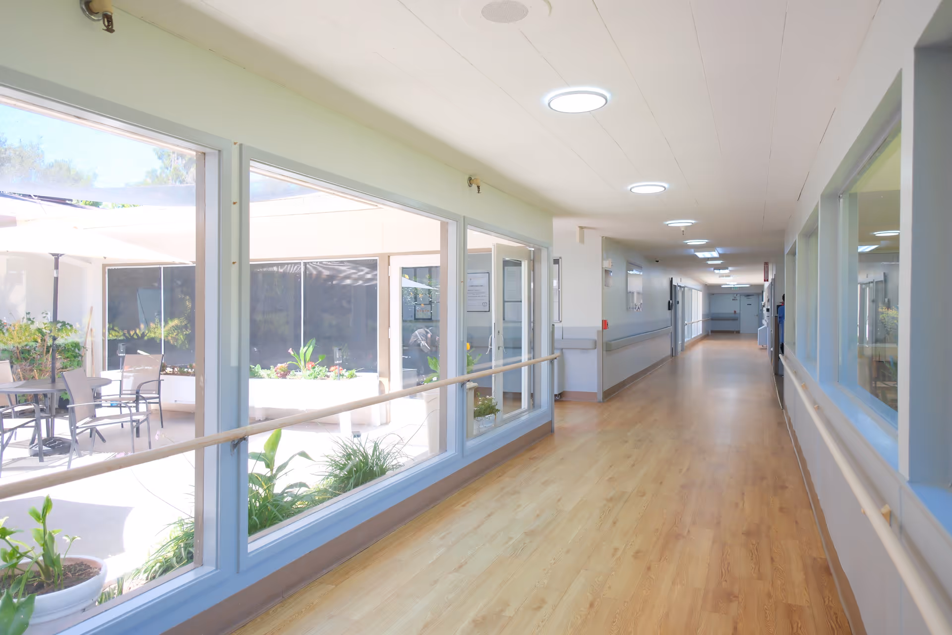 Bright interior hallway in a senior living facility with large windows and outdoor courtyard.