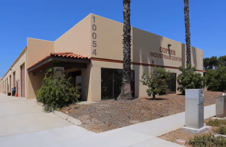 Exterior view of a beige building with palm trees and signage.