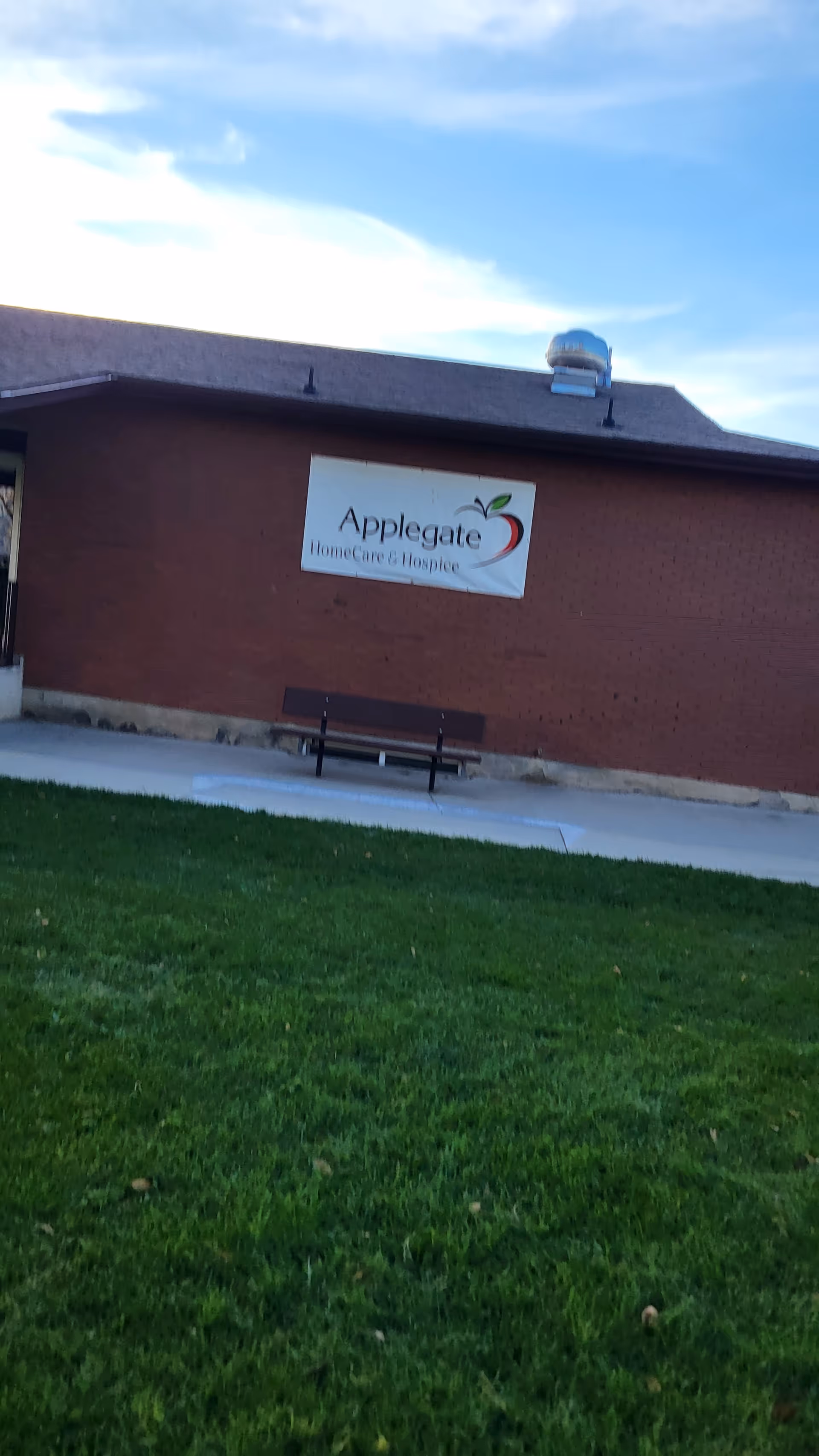 Brick building exterior with a sign reading Applegate HomeCare and Hospice and a bench.