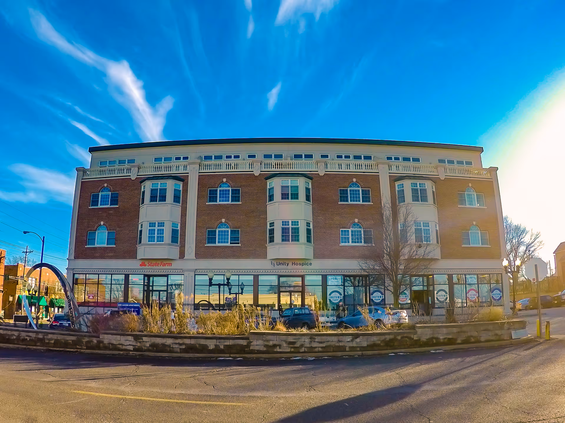 Front of a brick, multi-story building housing Unity Hospice storefronts and parked cars.