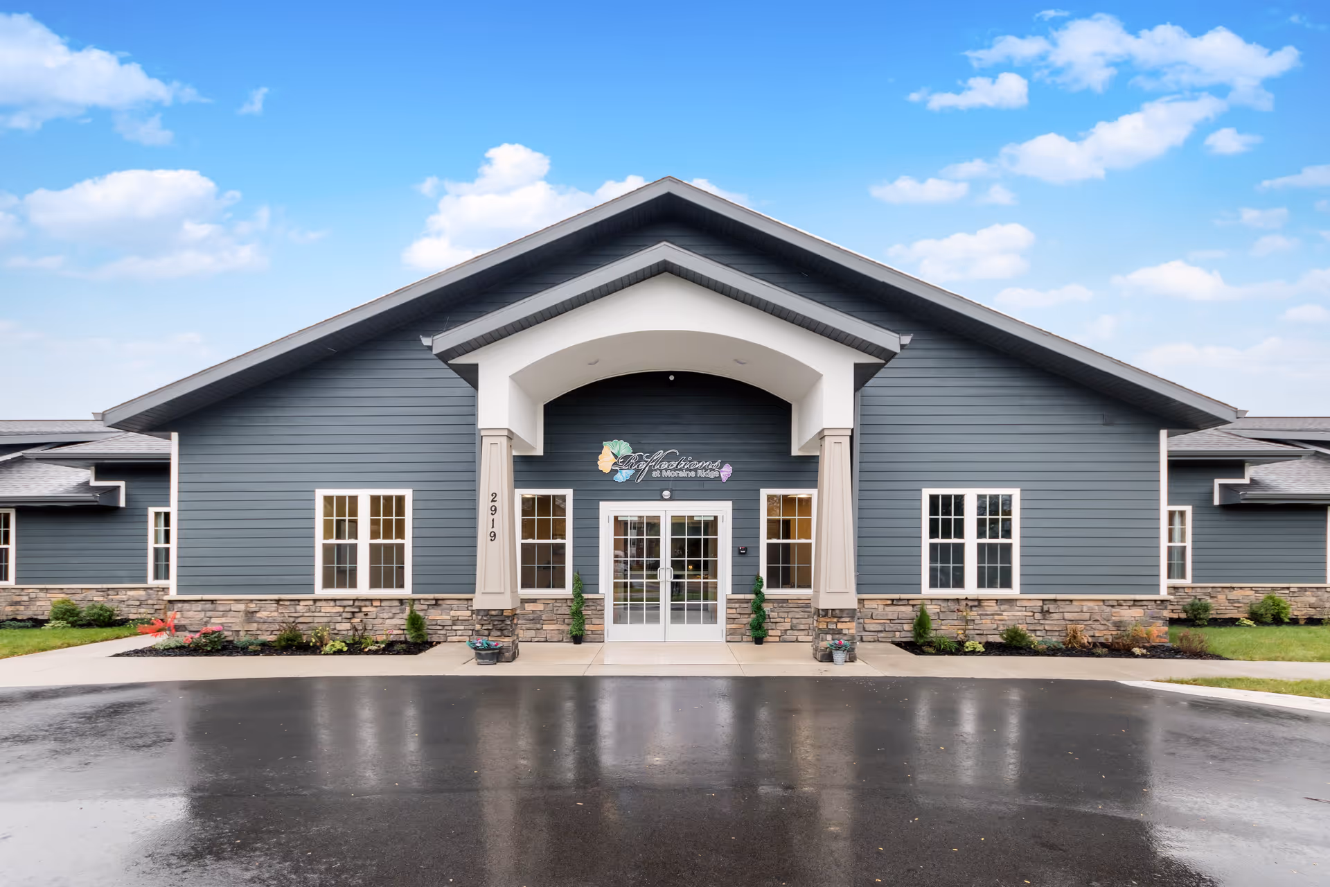 Front view of Reflections at Moraine Ridge Memory Care building, featuring blue siding and stone accents.