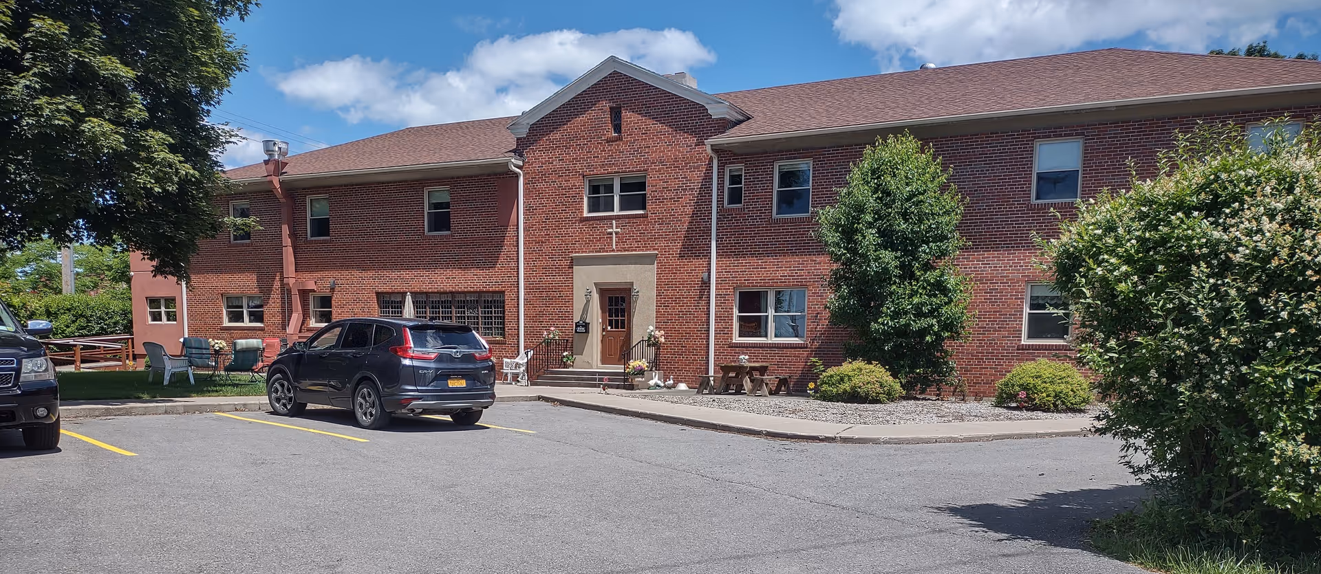 Brick senior living facility seen from the front with parked cars and landscaping.