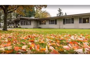 A single-story senior living facility exterior with a green lawn and autumn leaves.