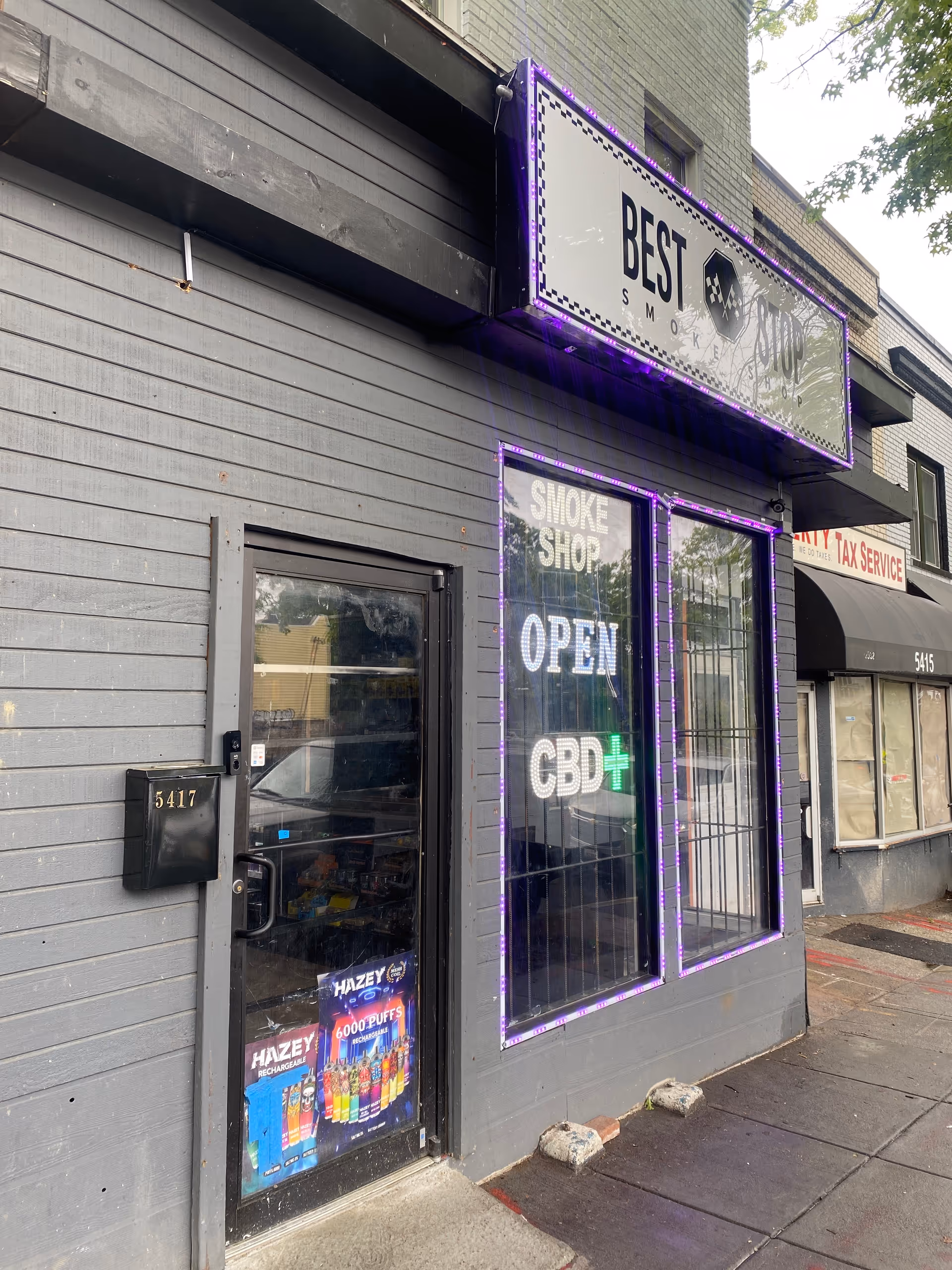 Exterior storefront with purple neon sign reading Best Stop Smoke Shop and Open CBD window.