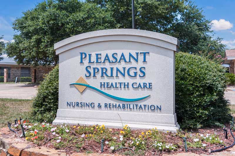 A Pleasant Springs Health Care sign with a landscaped flower bed in front.