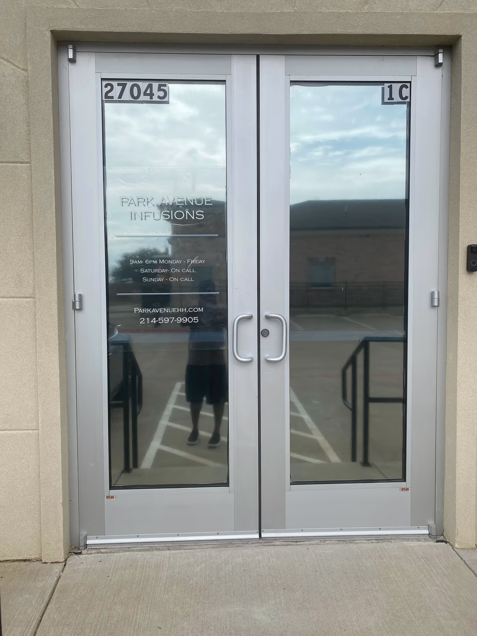 Glass double doors with Park Avenue Infusions sign at building entrance, reflecting surroundings.
