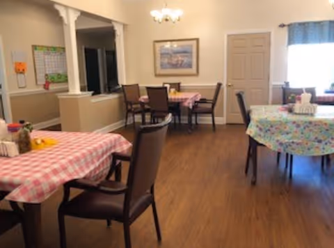 Dining room with pink-checkered and floral tablecloths, chairs, and a window.