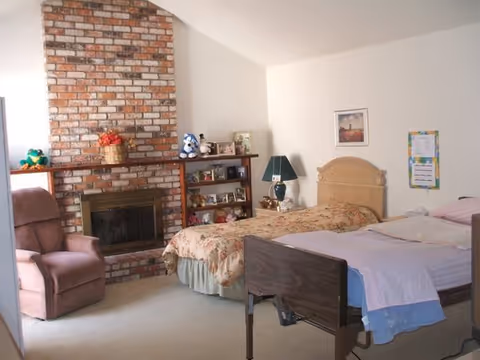 A cozy bedroom featuring two beds, a brick fireplace, and a recliner.