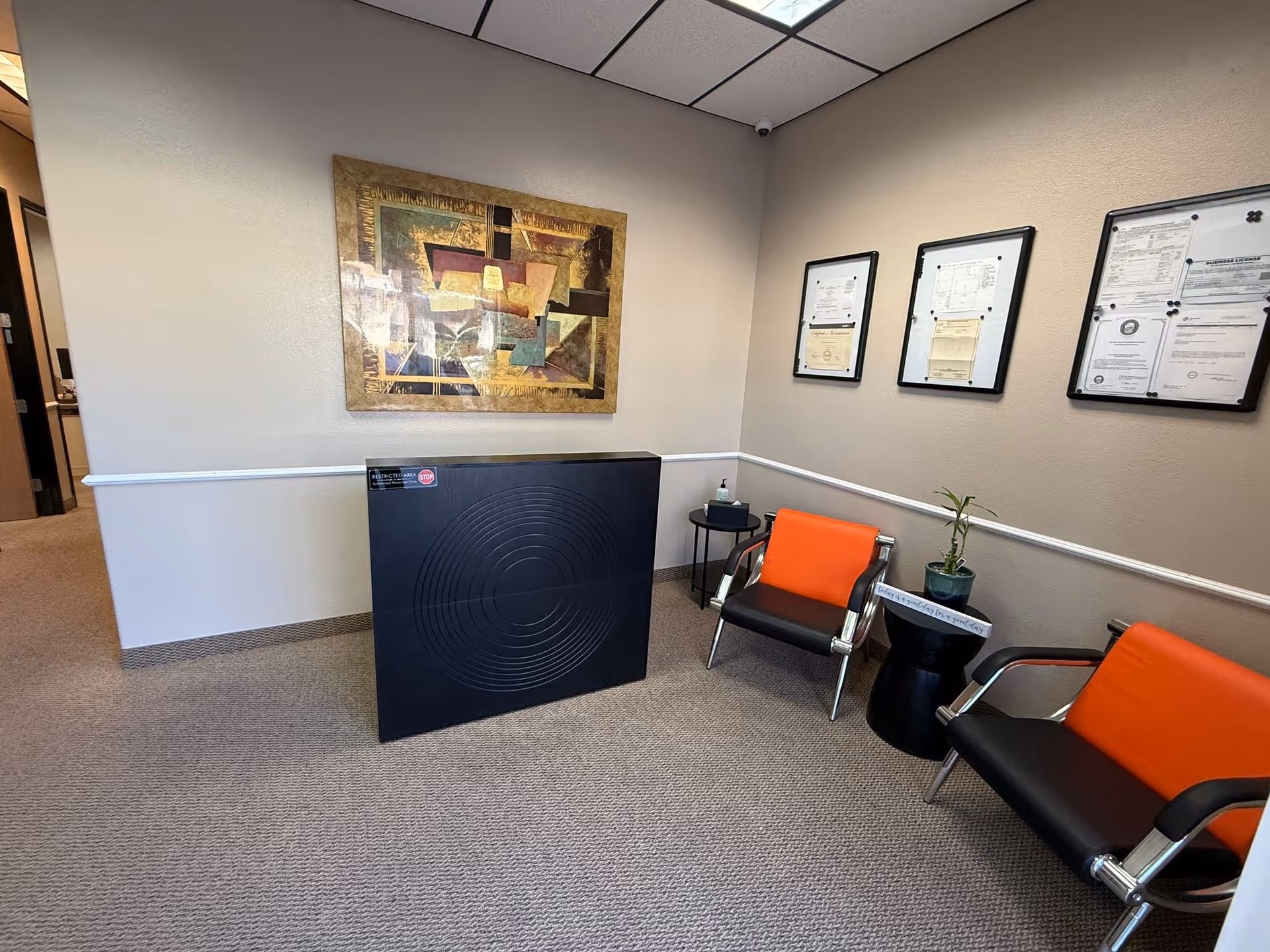 A waiting area inside a senior facility with orange chairs, wall art, and plants.