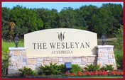 Large stone sign for The Wesleyan at Estrella with manicured landscaping and trees behind.