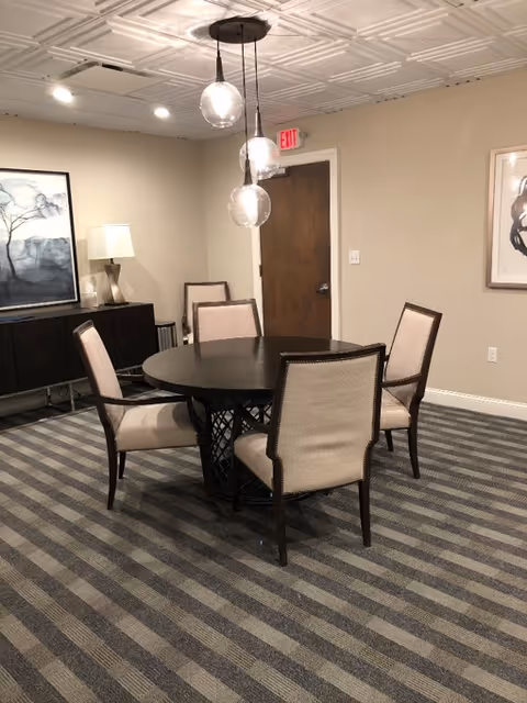 Round dark dining table with beige chairs in a furnished senior living dining room.